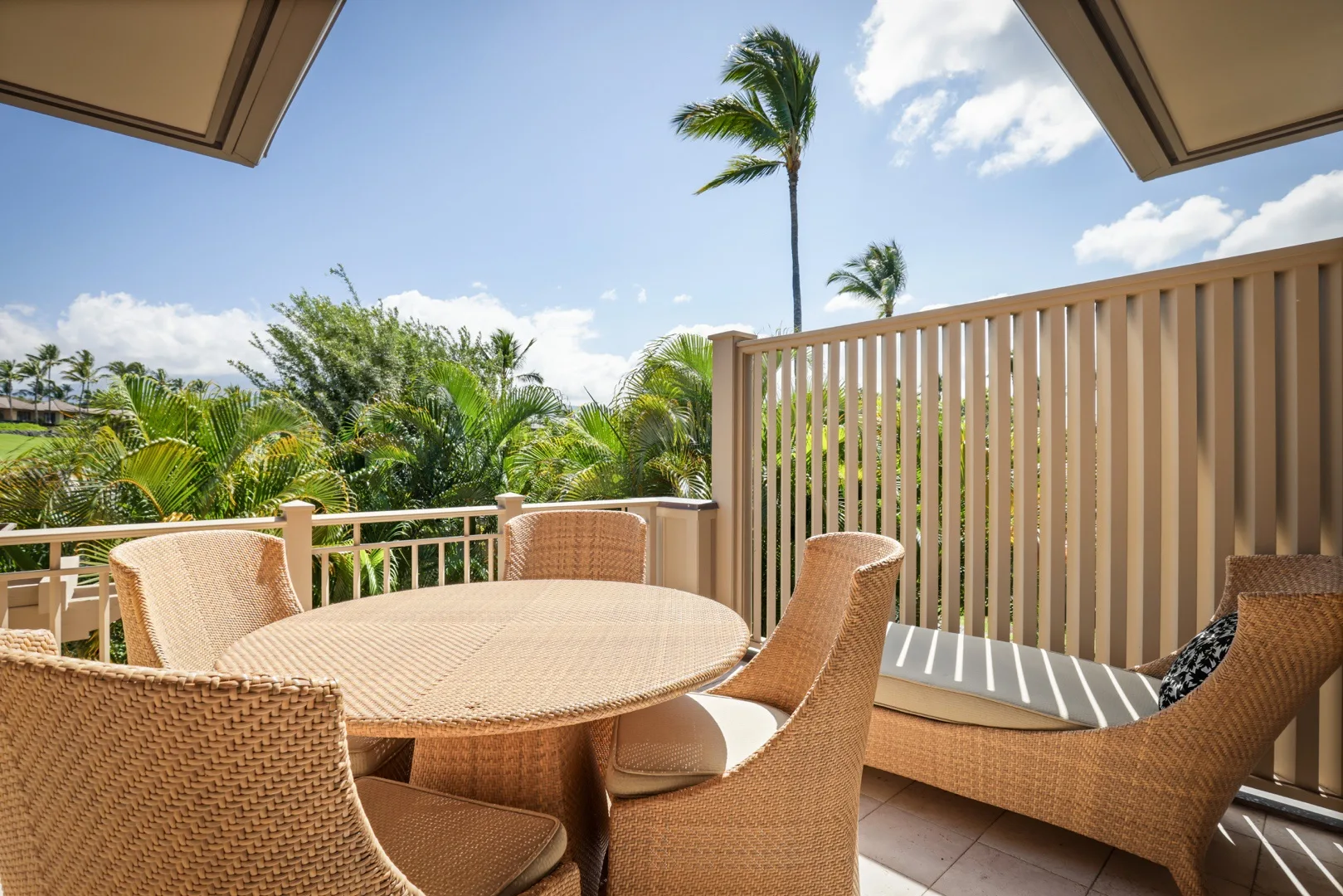 Una zona de estar en un balcón con una mesa redonda da a vegetación tropical y palmeras.