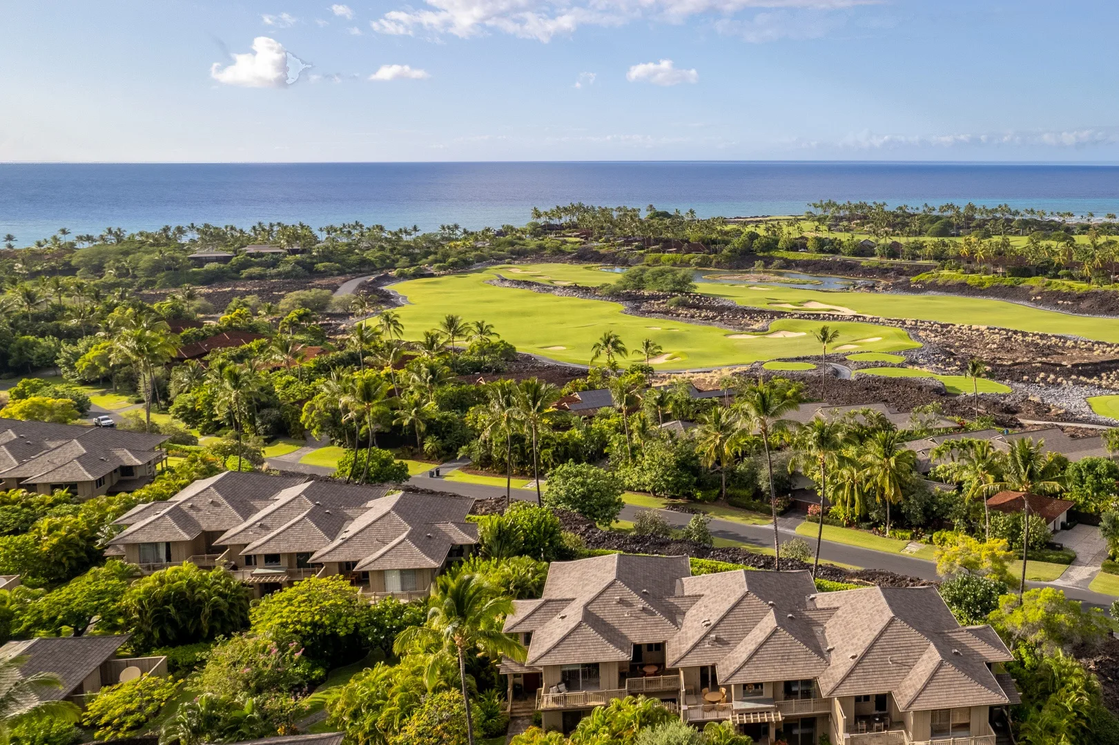 Vista aérea de casas entre vegetación tropical, junto a un campo de golf y el océano.
