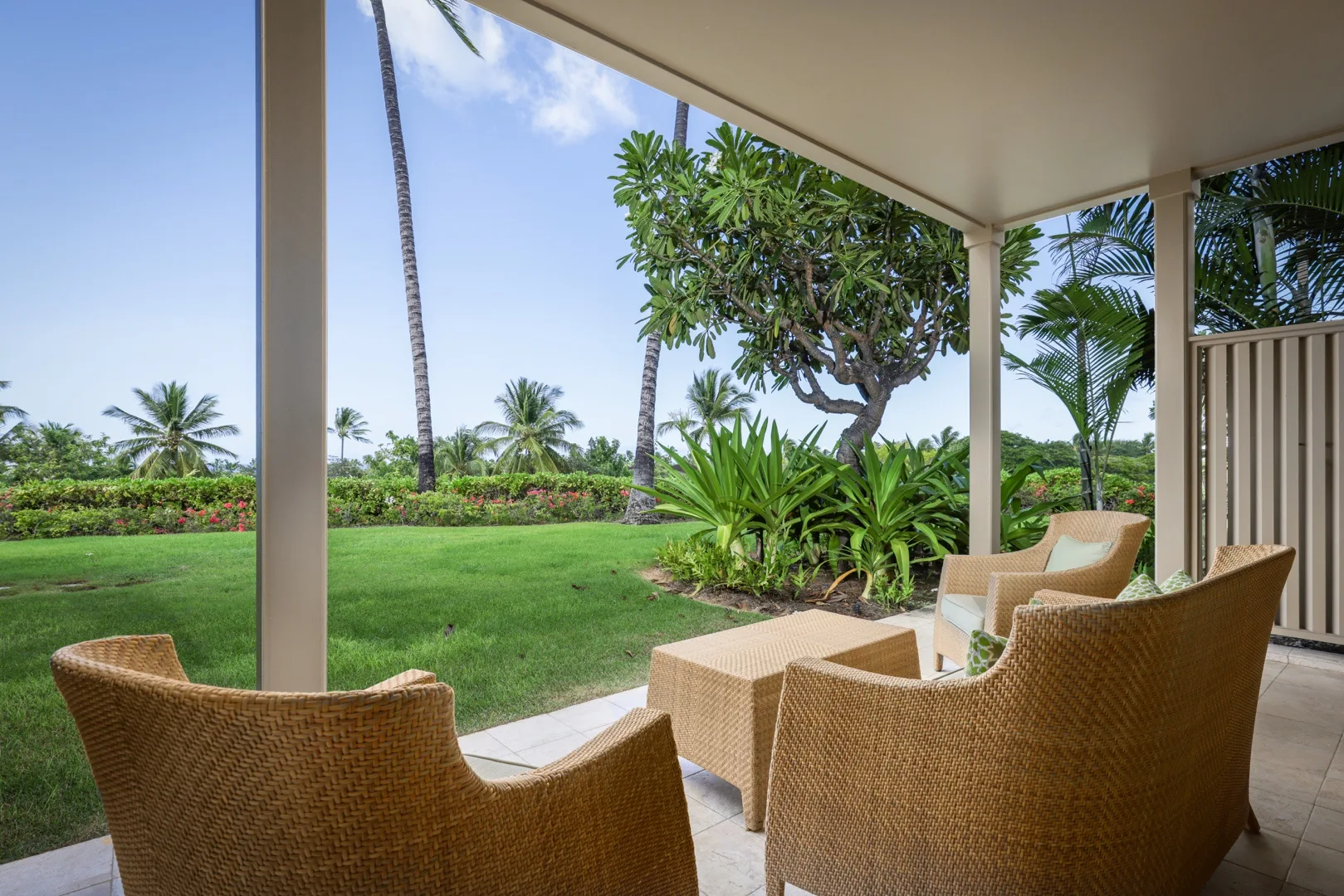 Una zona de estar en una terraza cubierta da a un césped verde y un jardín tropical.