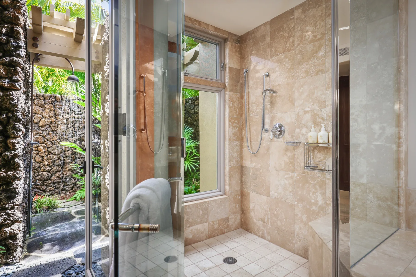 Una zona de ducha con azulejos, paneles de vidrio y una ventana con vista a la vegetación.