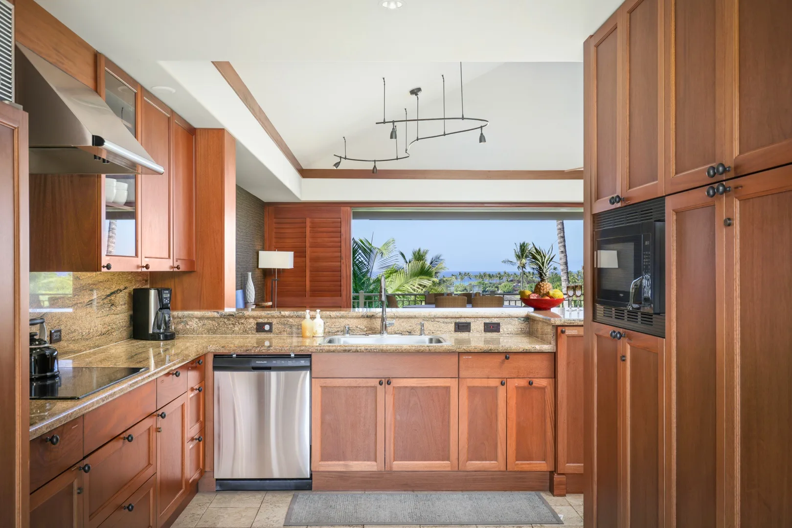 Una cocina con gabinetes de madera y una ventana amplia con vista a palmeras.