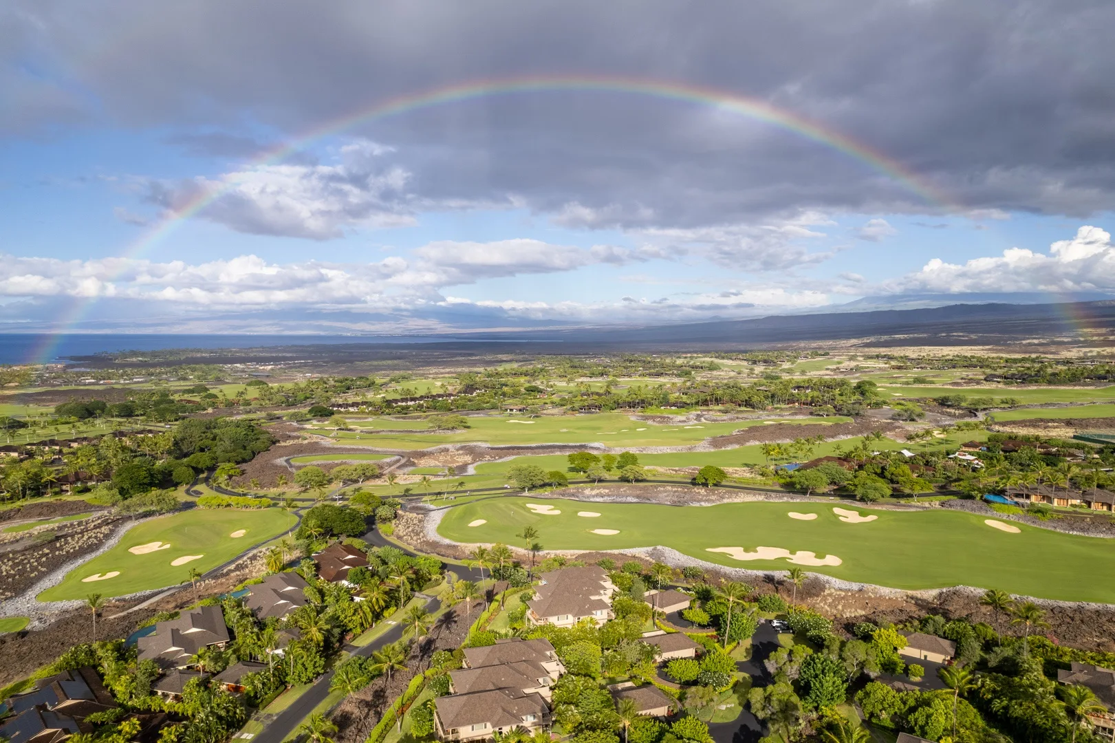 Vista aérea de un campo de golf y vegetación circundante bajo un arcoíris.