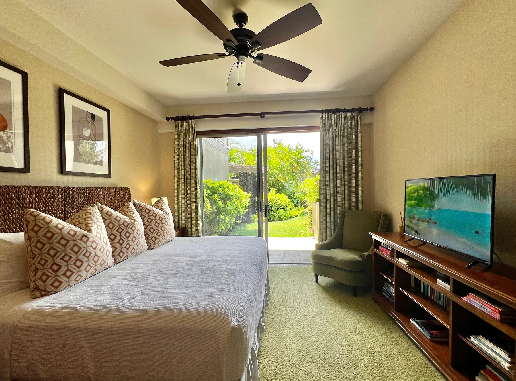 Un dormitorio con una cama, asientos y un televisor frente a una vista luminosa del jardín.