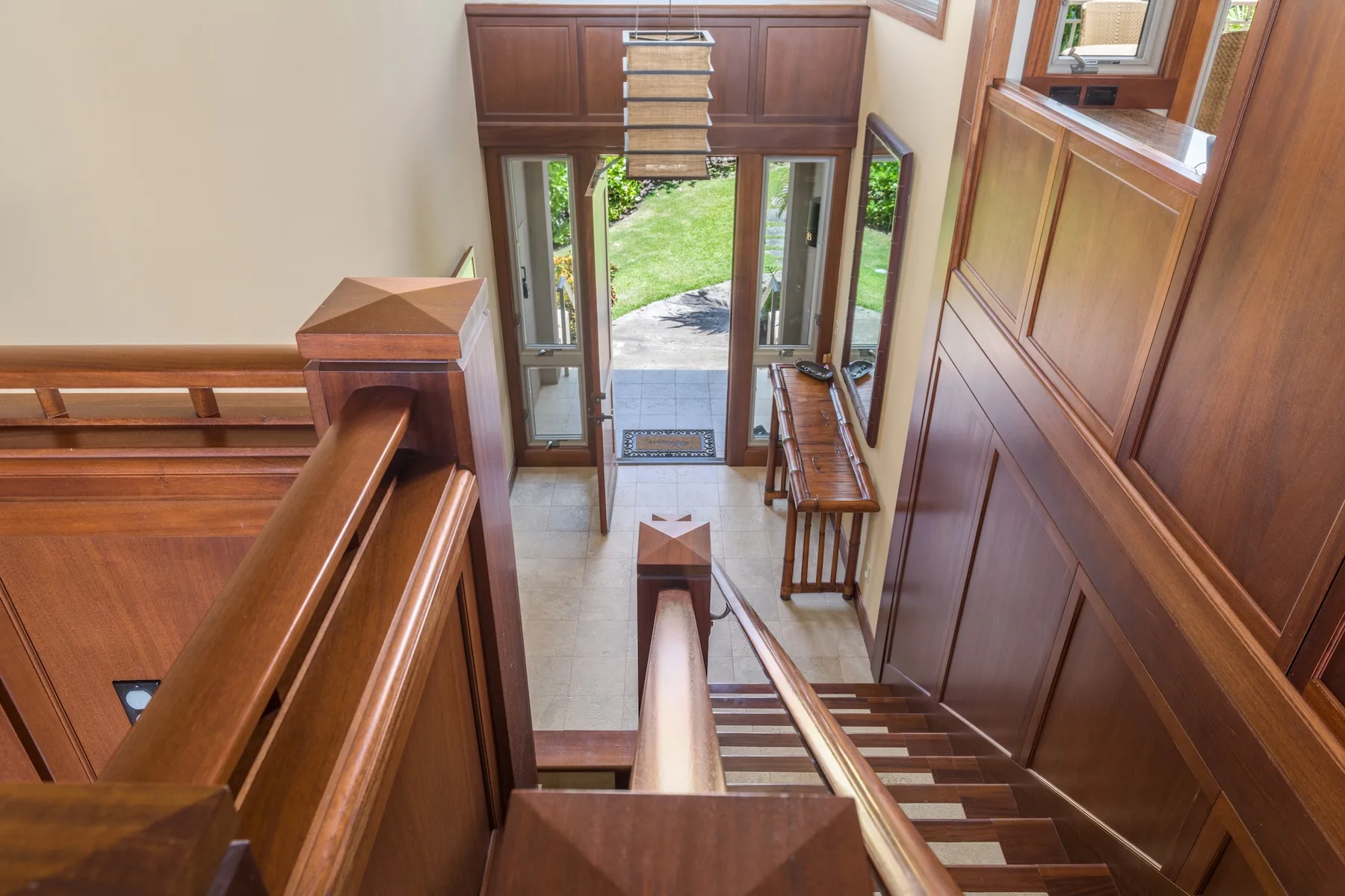 Una escalera de madera desciende por una entrada amplia hacia una puerta de vidrio.