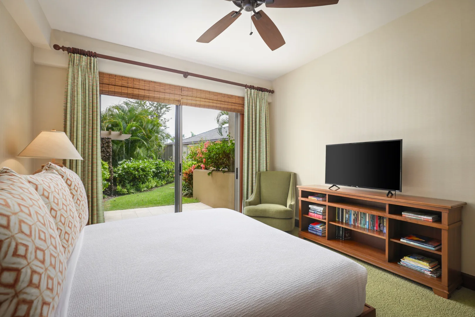 Un dormitorio con cama, televisor y puertas corredizas de vidrio que dan a un jardín.