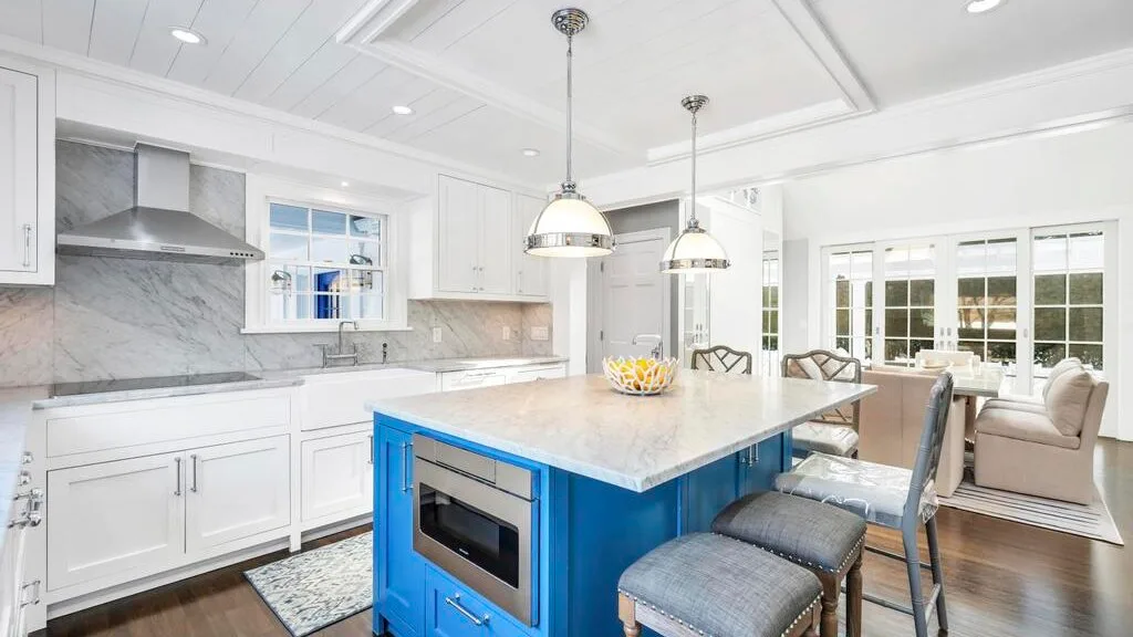 A bright kitchen with a blue island and pendant lights.