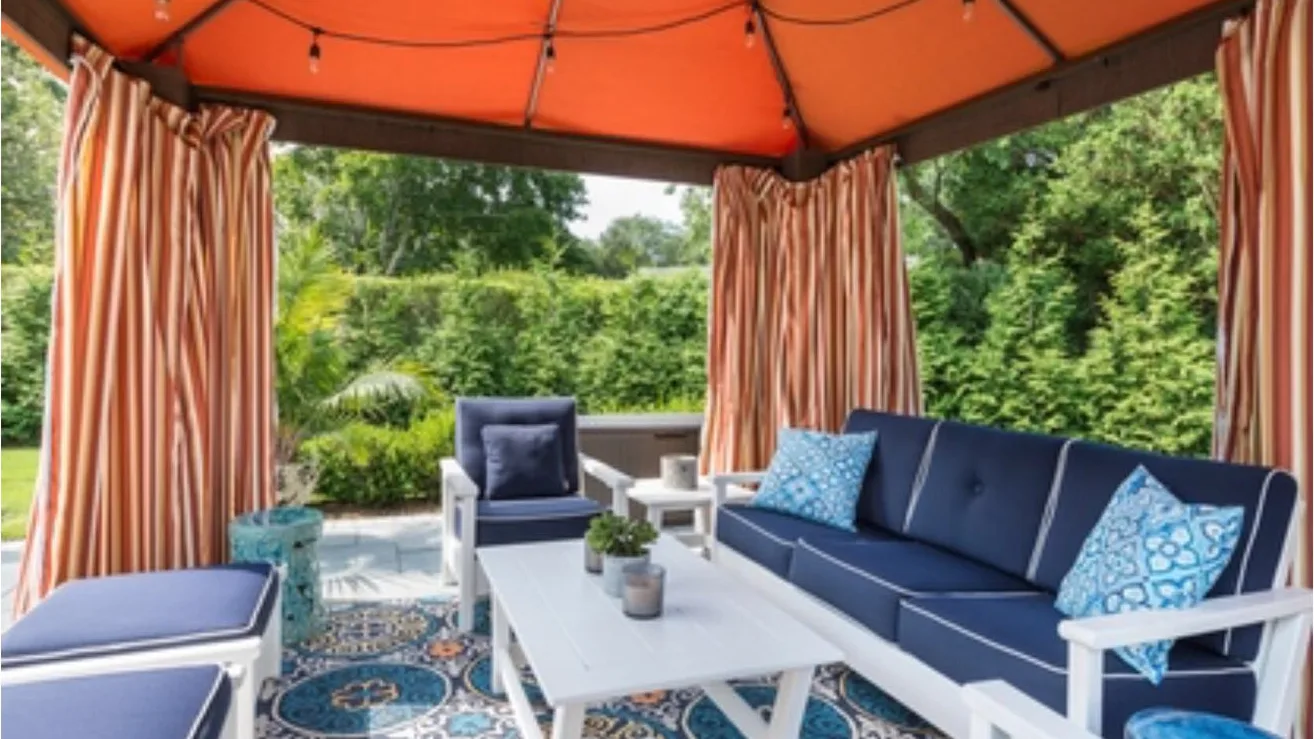 An outdoor seating area beneath an orange canopy, surrounded by greenery.