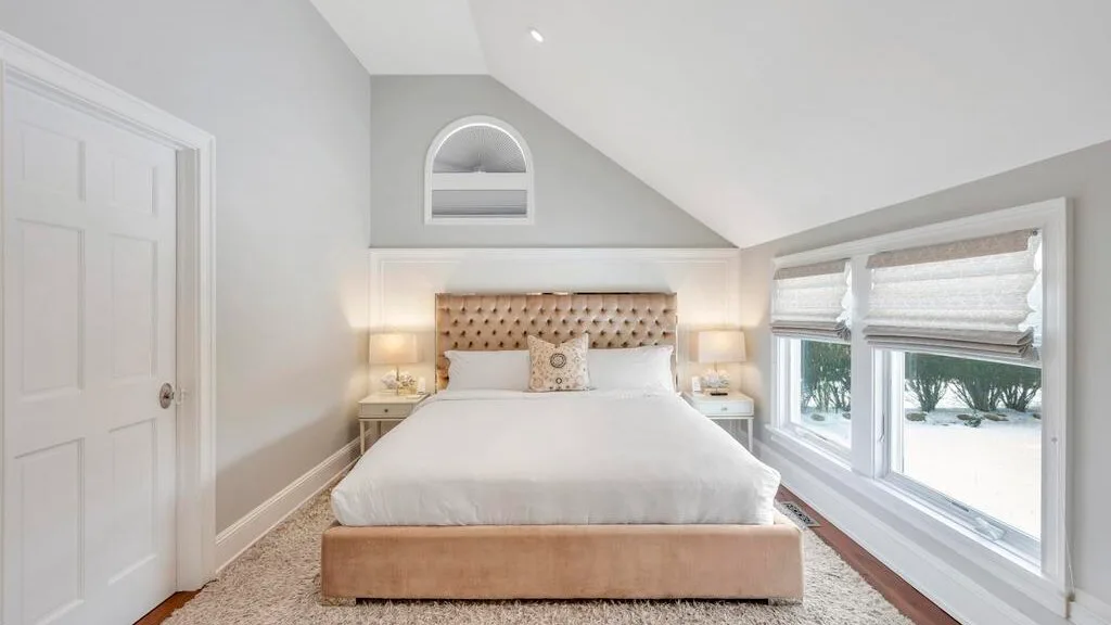 A bedroom with a bed beneath a sloped ceiling and windows along one wall.