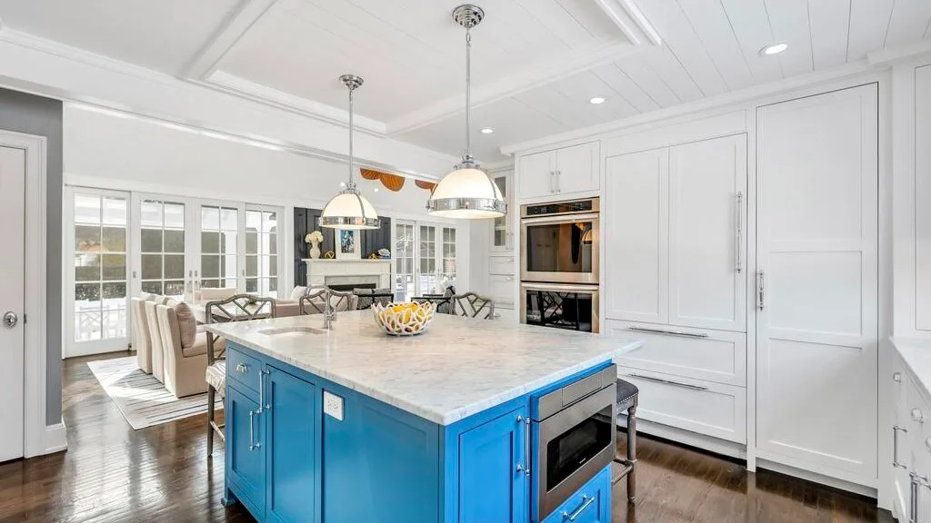A bright kitchen features a blue island with a light countertop.