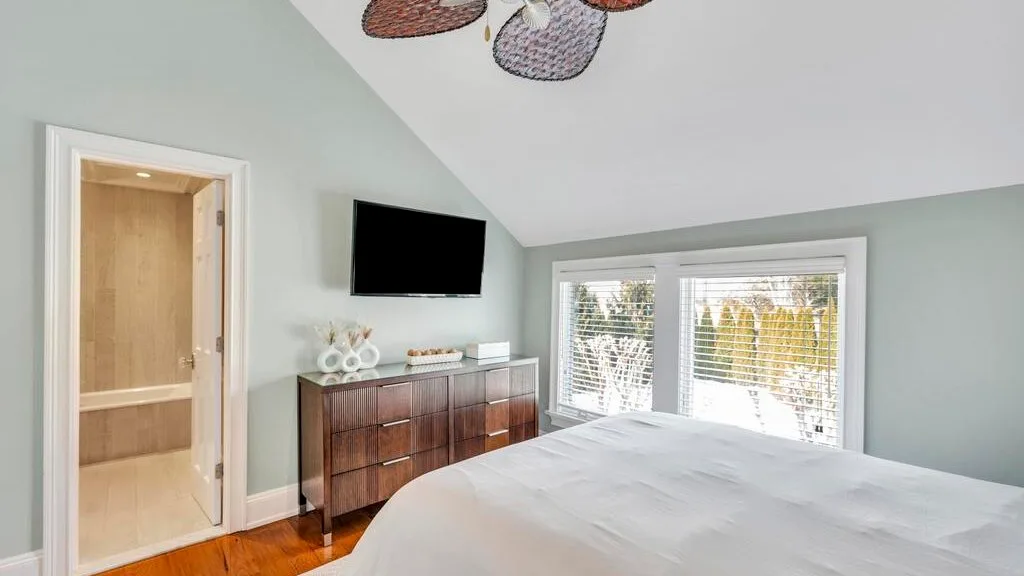 A bedroom with a bed, a television, and windows with blinds.