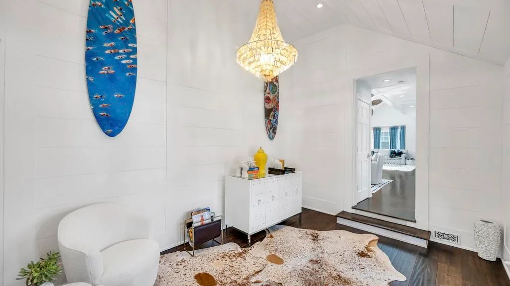 A bright living room has white seating, a patterned rug, and decorative wall art.