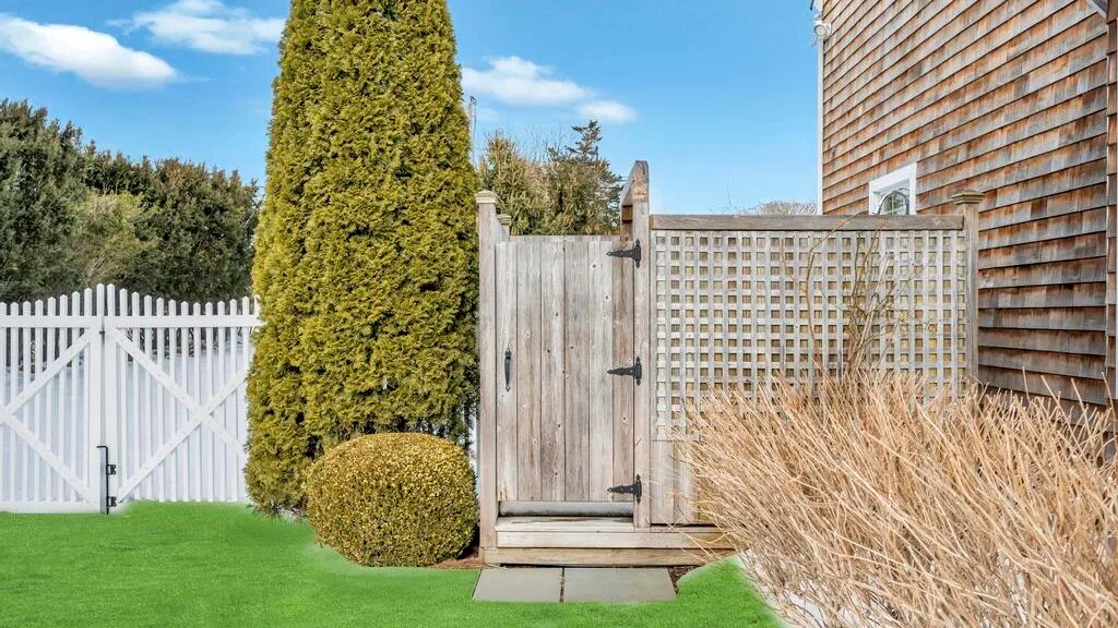 An outdoor garden area with a wooden gate, white fence, and green lawn.