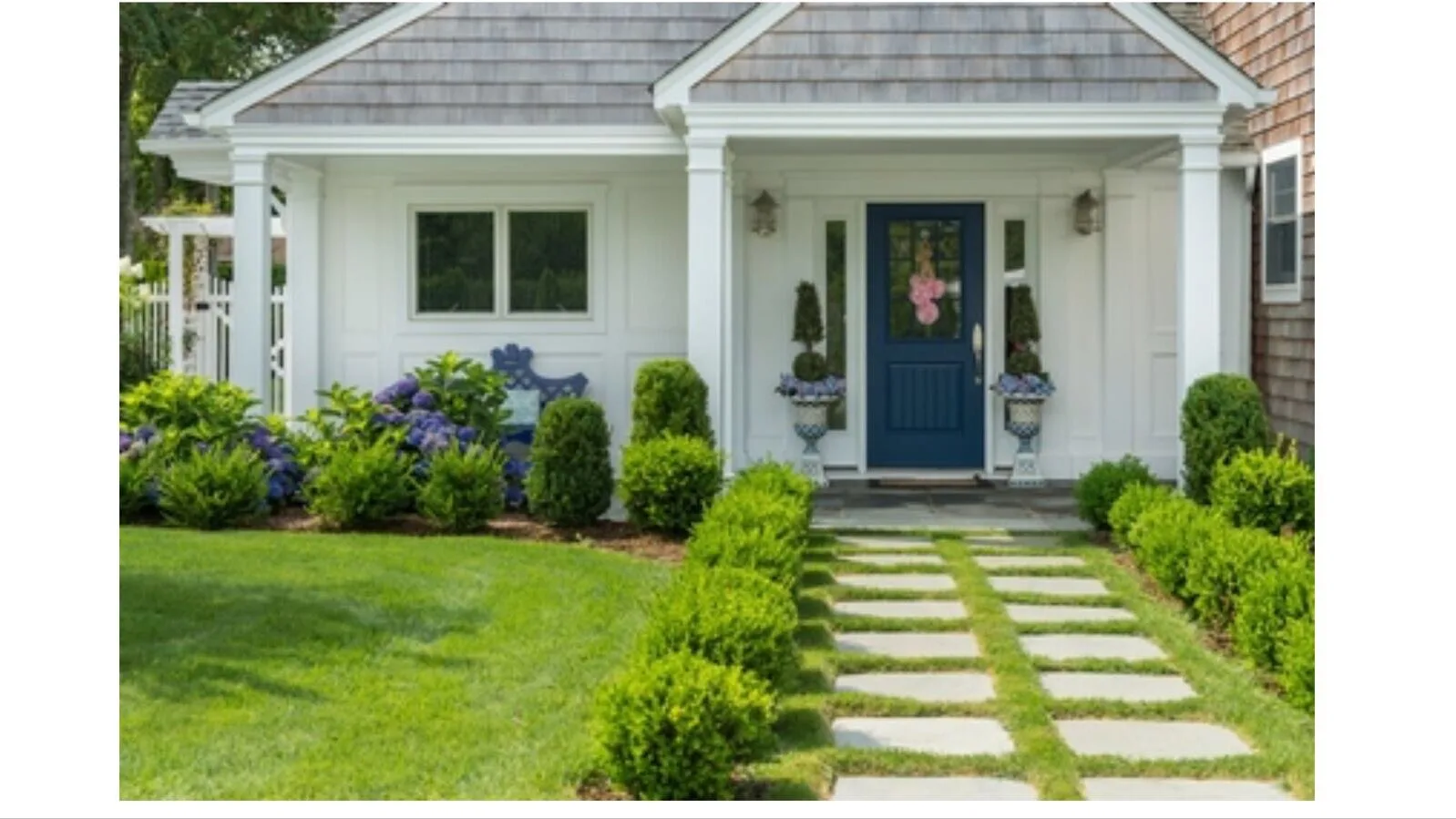 A white house entrance with a blue door, garden beds, and a stepping-stone path.