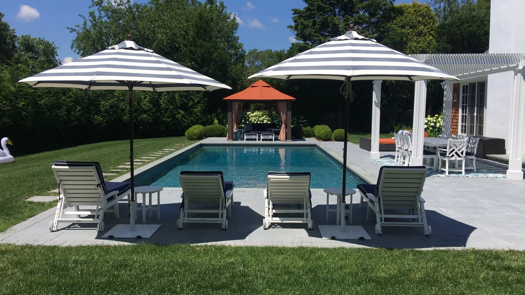 An outdoor swimming pool beside a patio with striped umbrellas and seating.