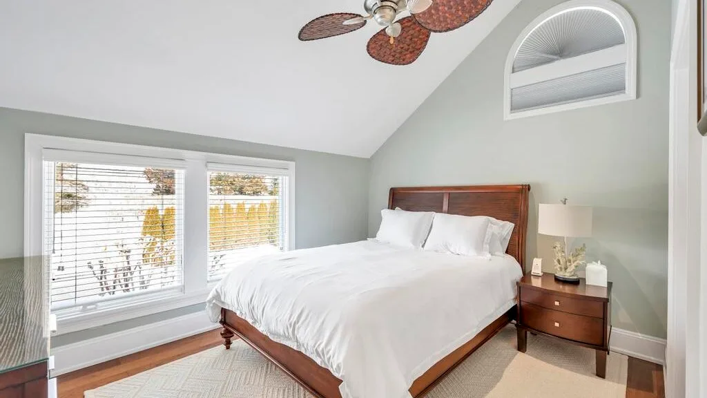 A bedroom with a wooden bed, white bedding, and windows with blinds.