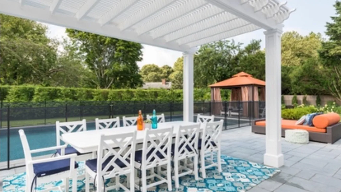 A covered outdoor dining area beside a swimming pool and garden.