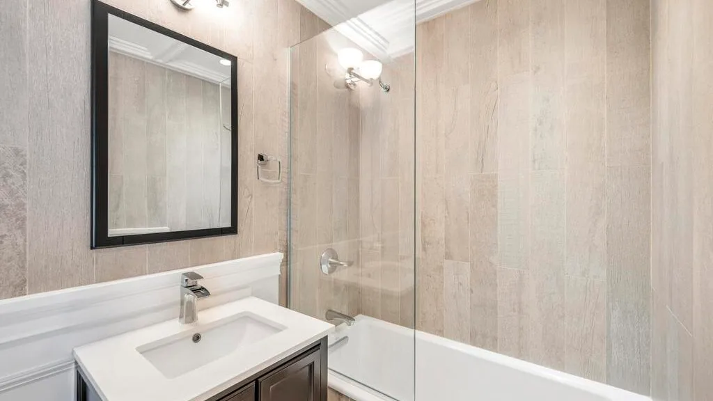 A bathroom with a sink, mirror, and bathtub behind a glass panel.
