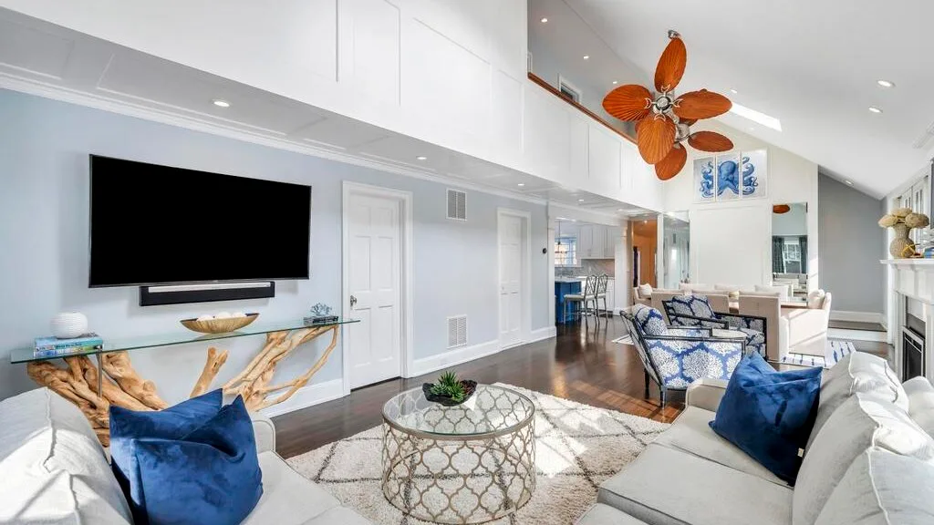 A bright living room with a television, seating, and a glass coffee table.