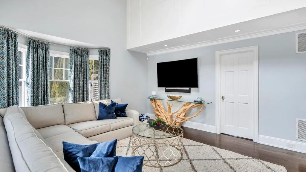 A living room with seating, a glass coffee table, and curtained windows.