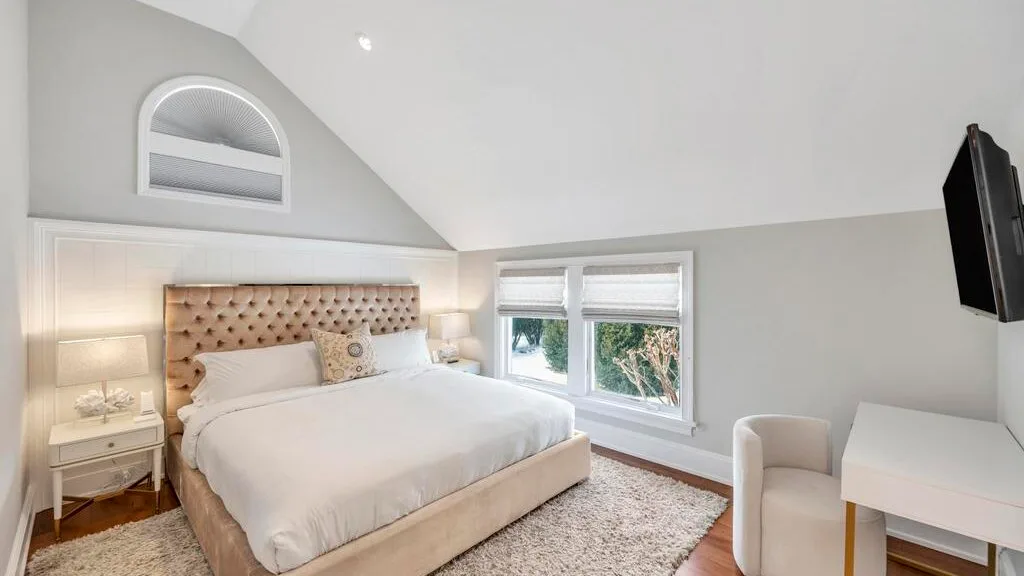 A bedroom with a bed beneath a sloped ceiling and windows beside it.