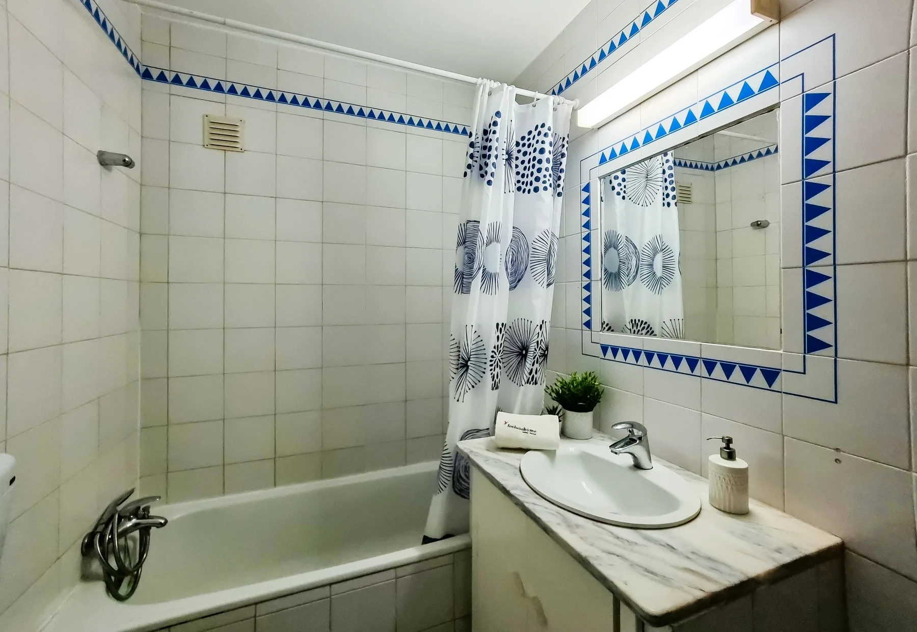 A tiled bathroom with a bathtub, shower curtain, and sink.