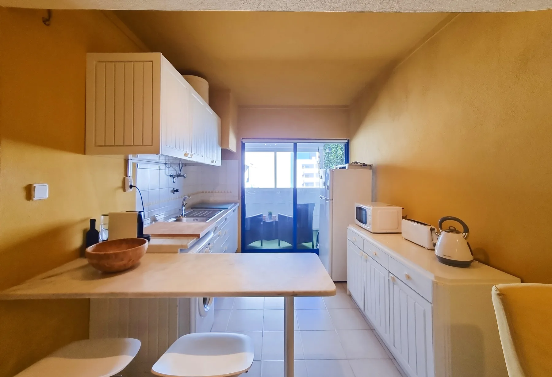 A narrow kitchen with cabinets, a countertop, and a glass door at the far end.