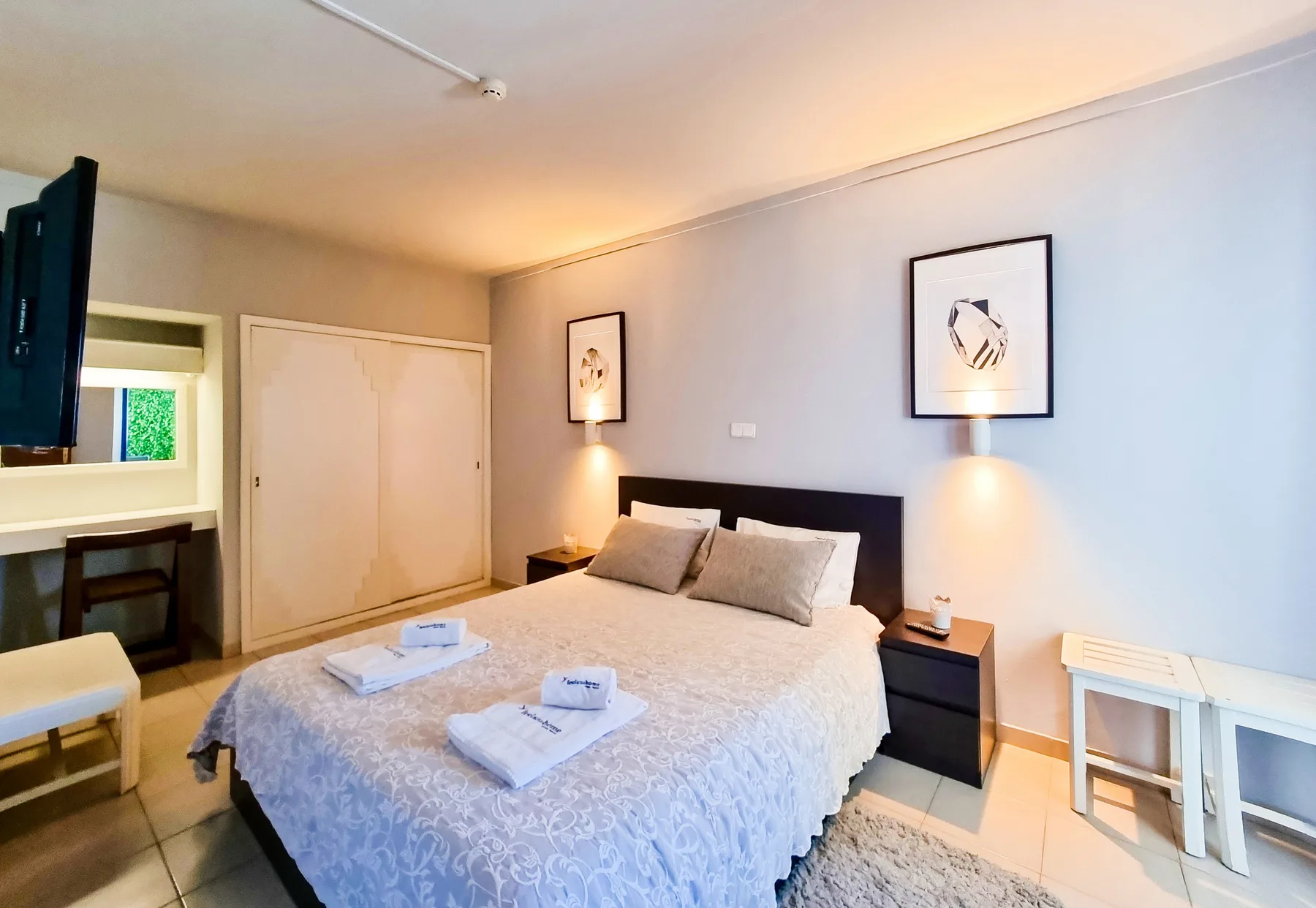 A bedroom with a double bed, bedside tables, and framed artwork.