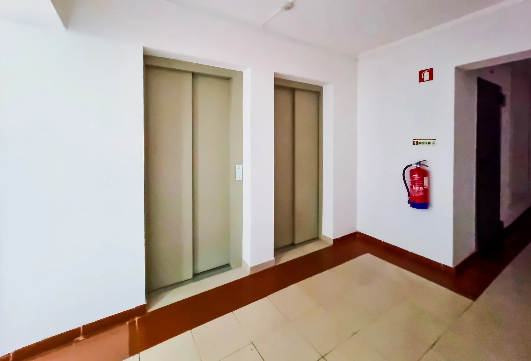 An indoor hallway with two elevator doors and a fire extinguisher.