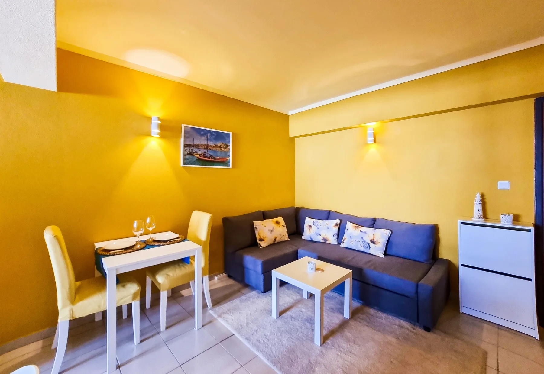 A living area with a dark sectional sofa, a small table, and a dining nook.