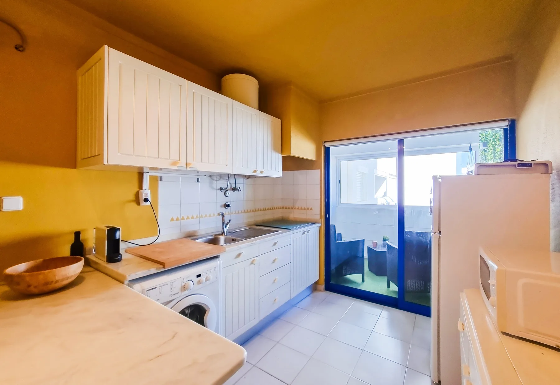 A compact kitchen with white cabinets and a sliding glass door opening onto a balcony.