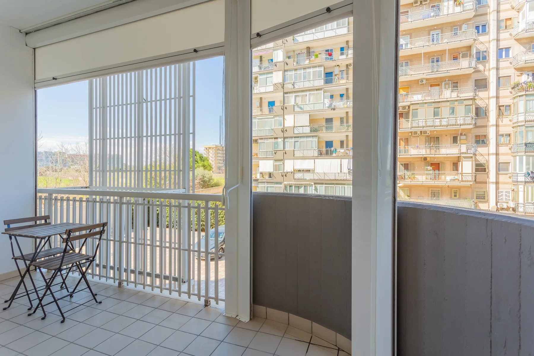 A balcony with a small table and seating overlooks nearby apartment buildings.