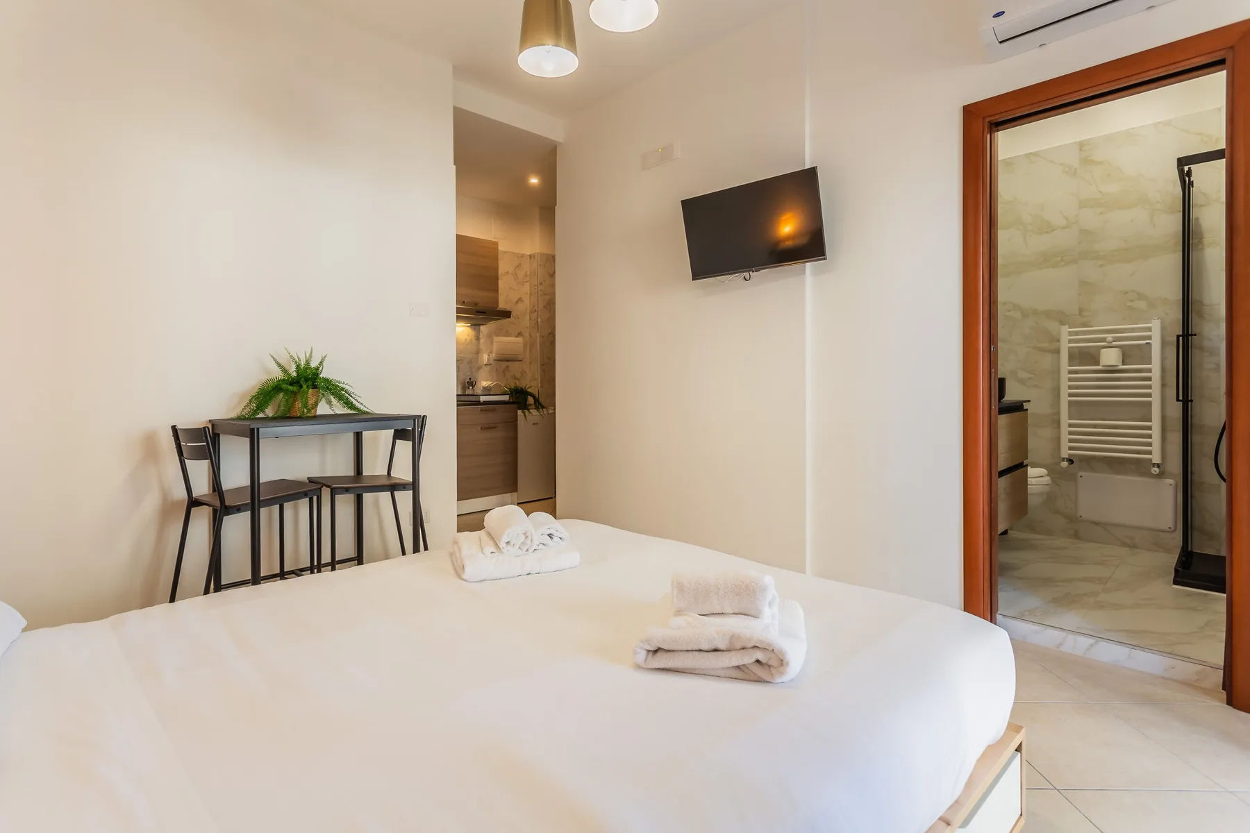 A bedroom with a neatly made bed, a small table, and a wall-mounted television.