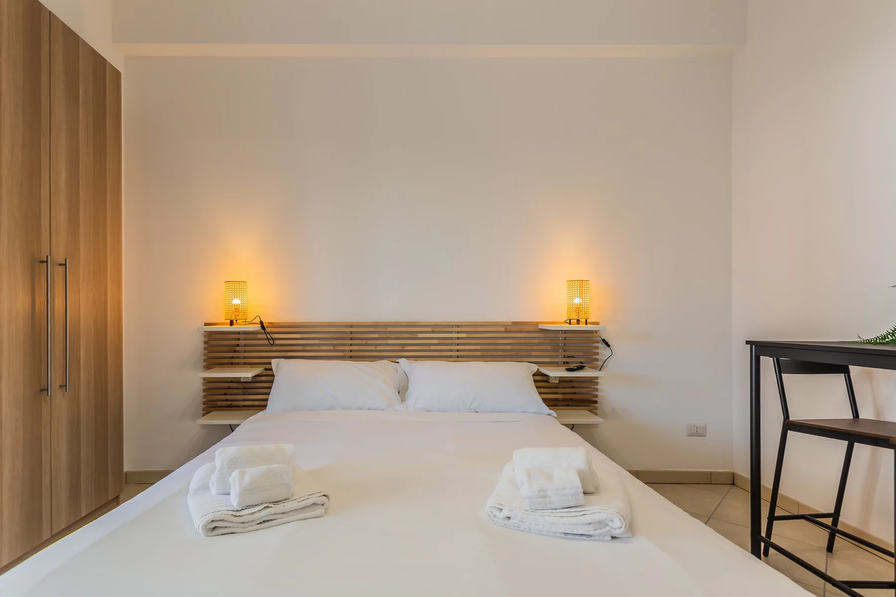 A bedroom with a neatly made bed and warm bedside lighting.