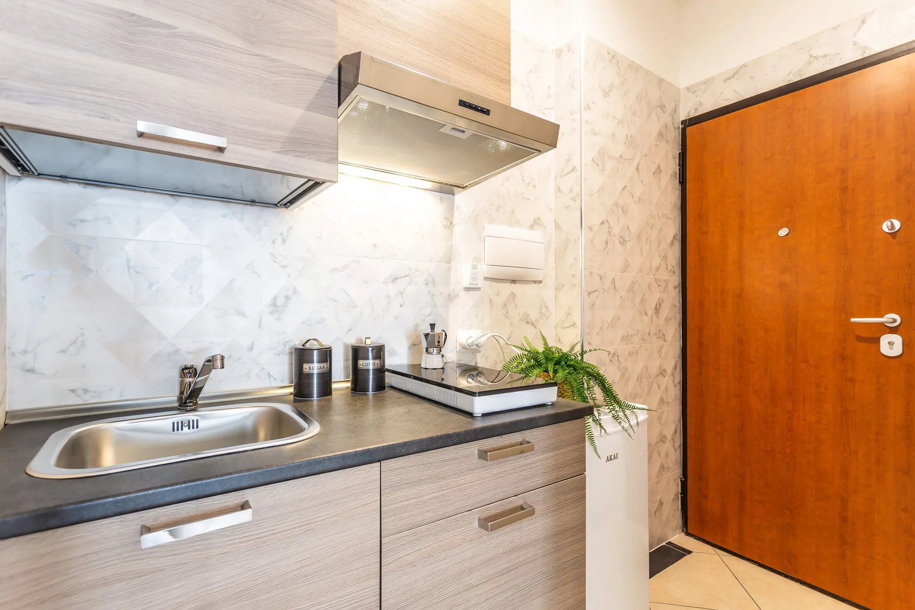 A compact kitchen counter with a sink and cooktop stands beside a wooden door.