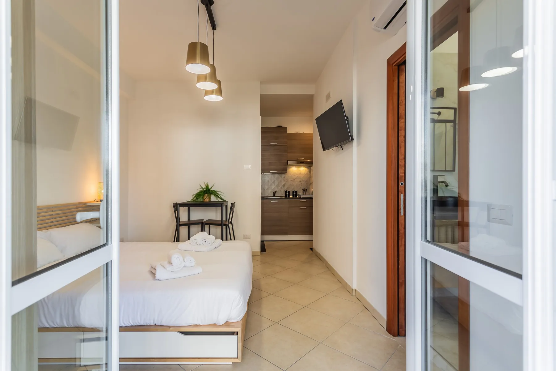 A bedroom with a neatly made bed and a small desk near the kitchenette.