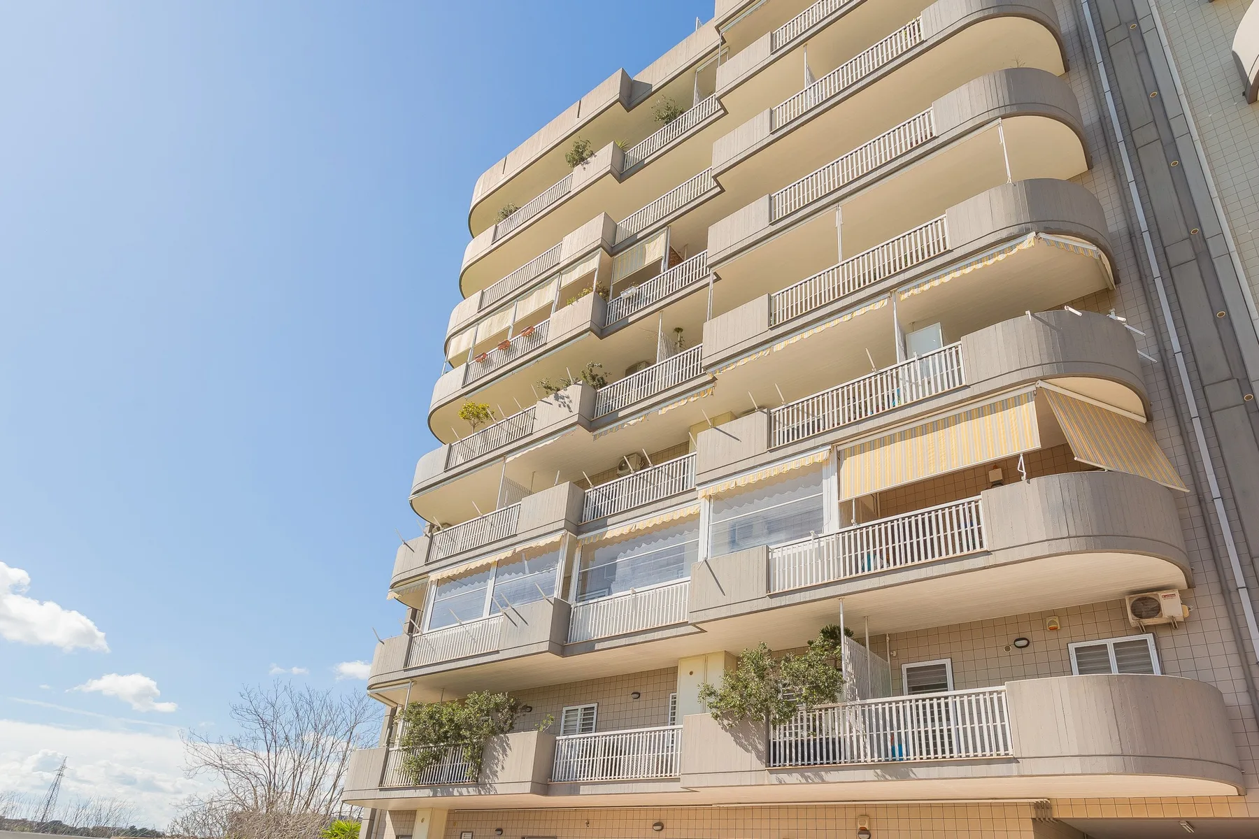A multi-story apartment building with curved balconies beneath a clear sky.