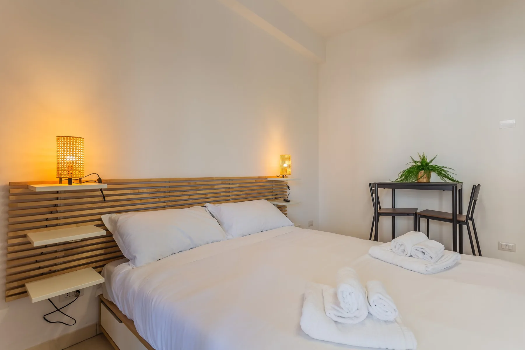 A bedroom with a bed, folded towels, and a small table with a plant.