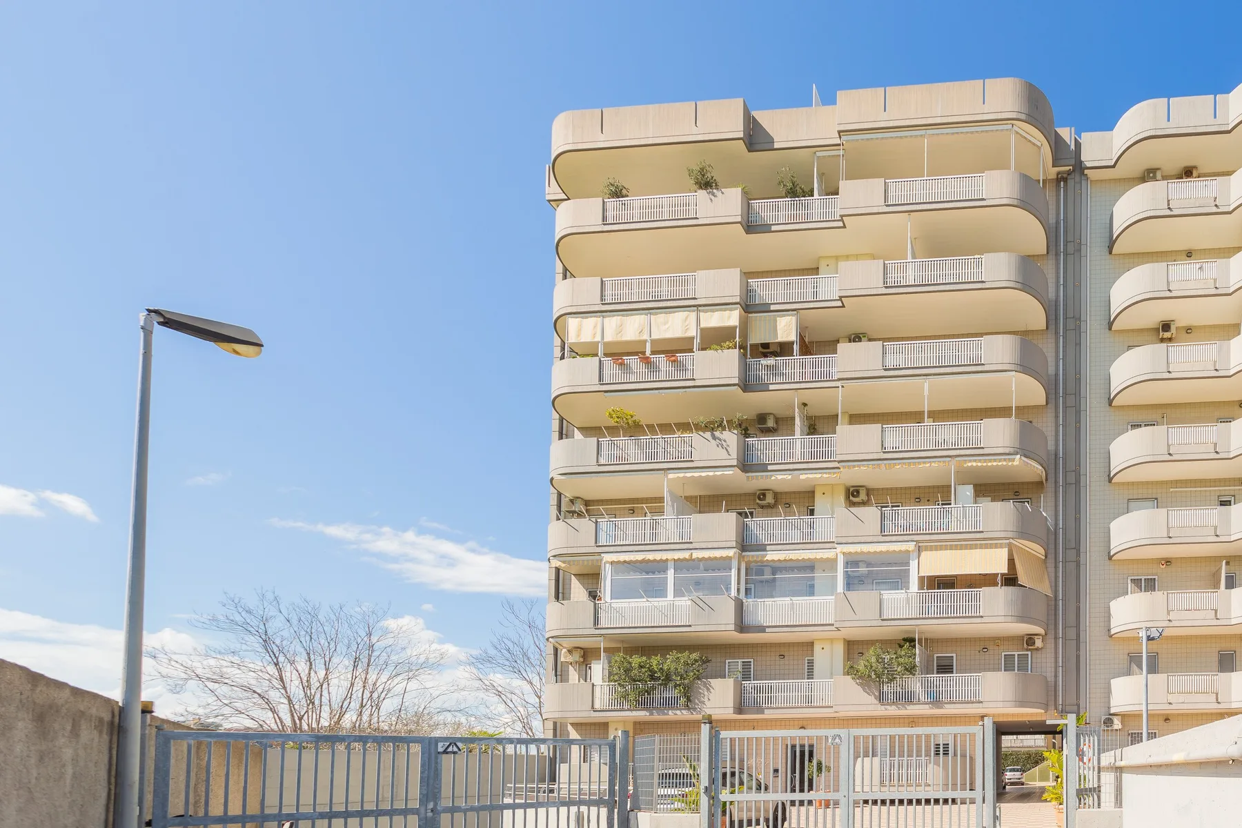 A residential apartment building stands behind a metal fence under a clear sky.
