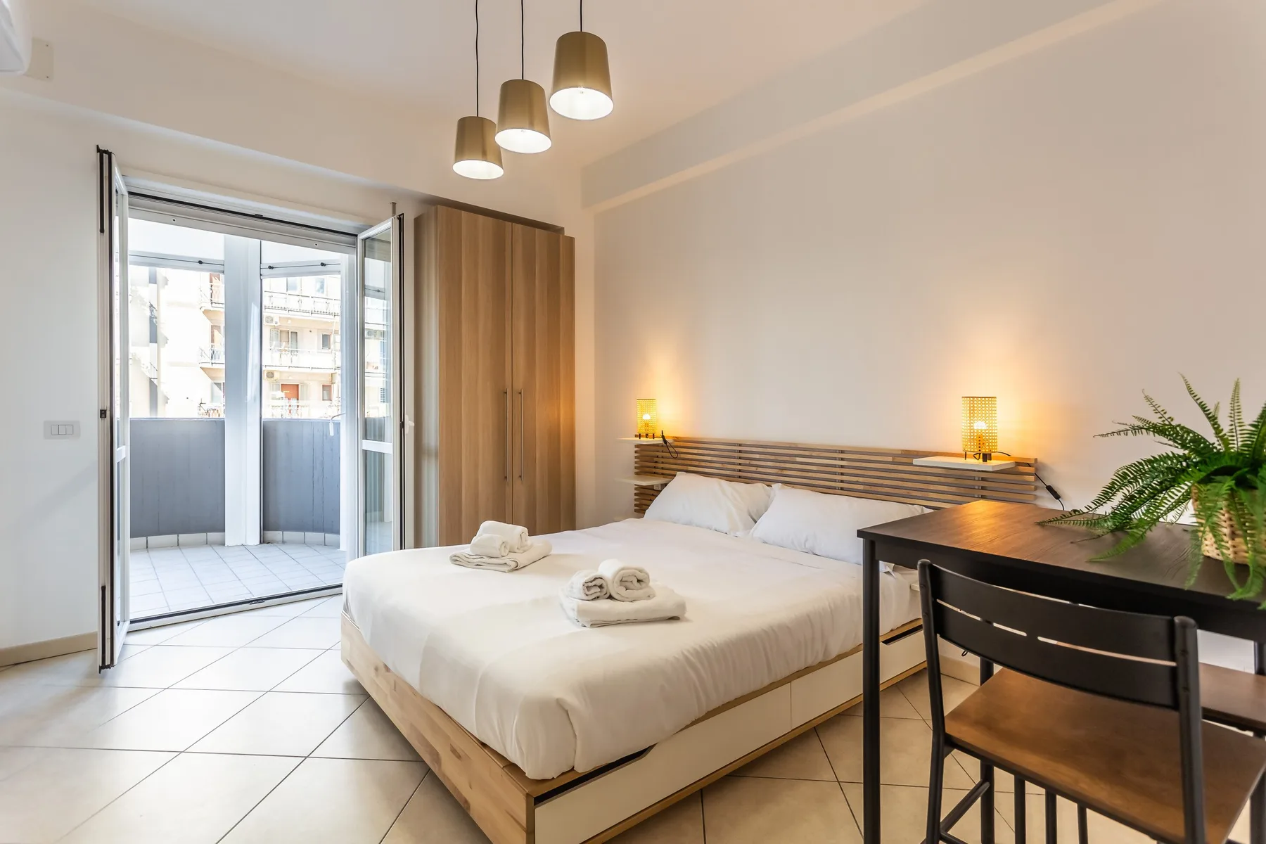 A bright bedroom with a bed, bedside lights, and a desk by the window.