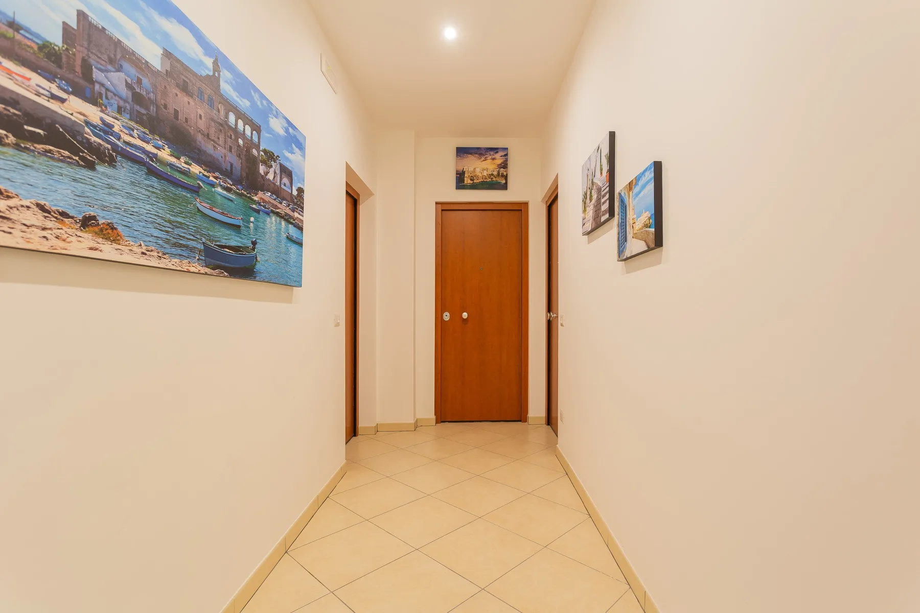 A tiled hallway with a wooden door and framed pictures on the walls.