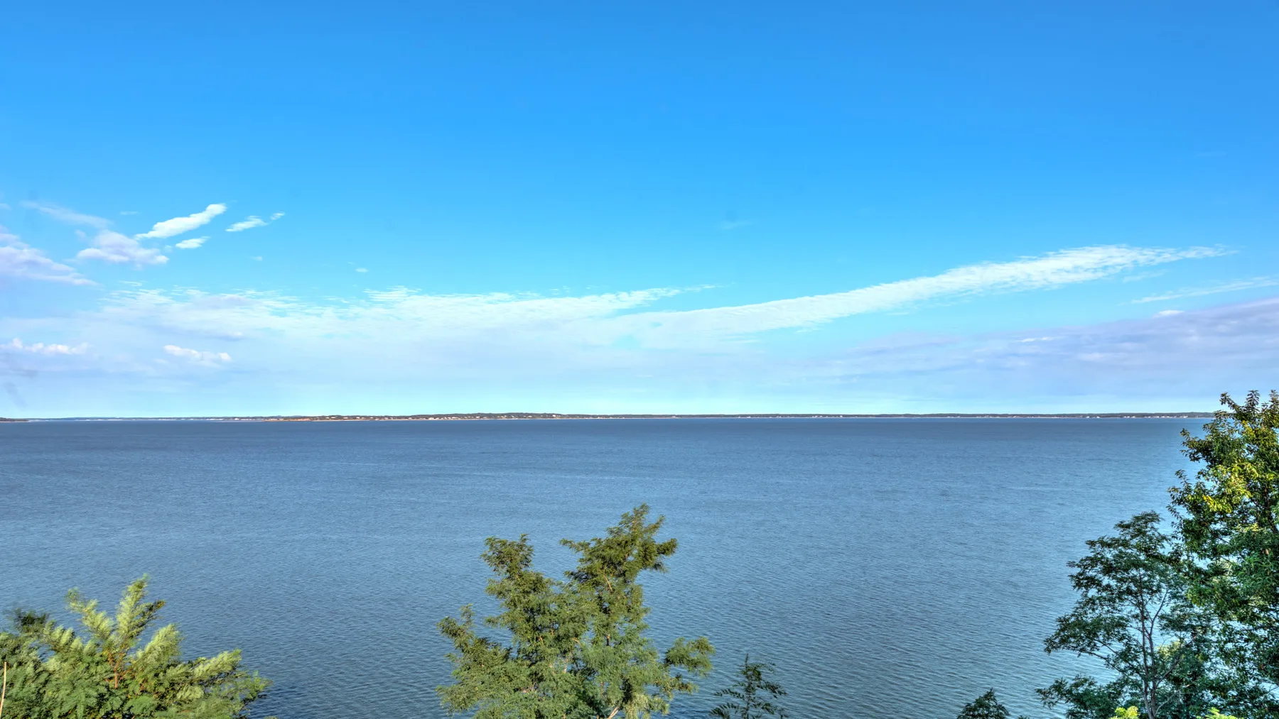 A wide body of water stretches beneath a clear blue sky, with trees along the shore.