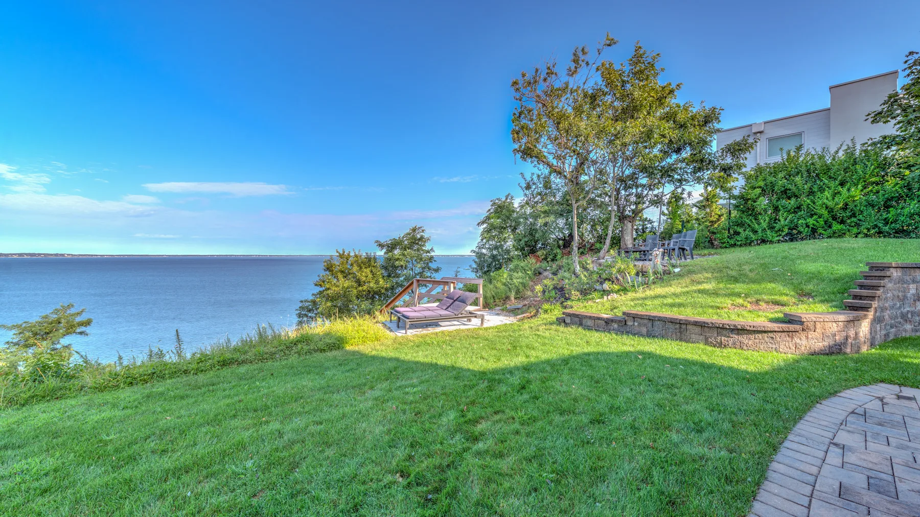 A grassy waterfront yard overlooks the water, with a small patio beside the trees.