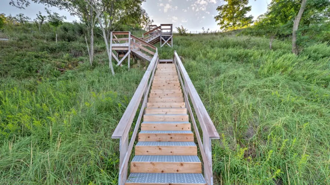 A wooden staircase with railings climbs through a grassy hillside.