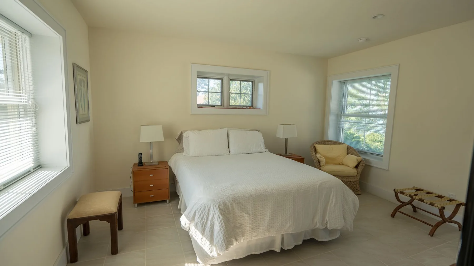 A bedroom with a neatly made bed and windows on three walls.