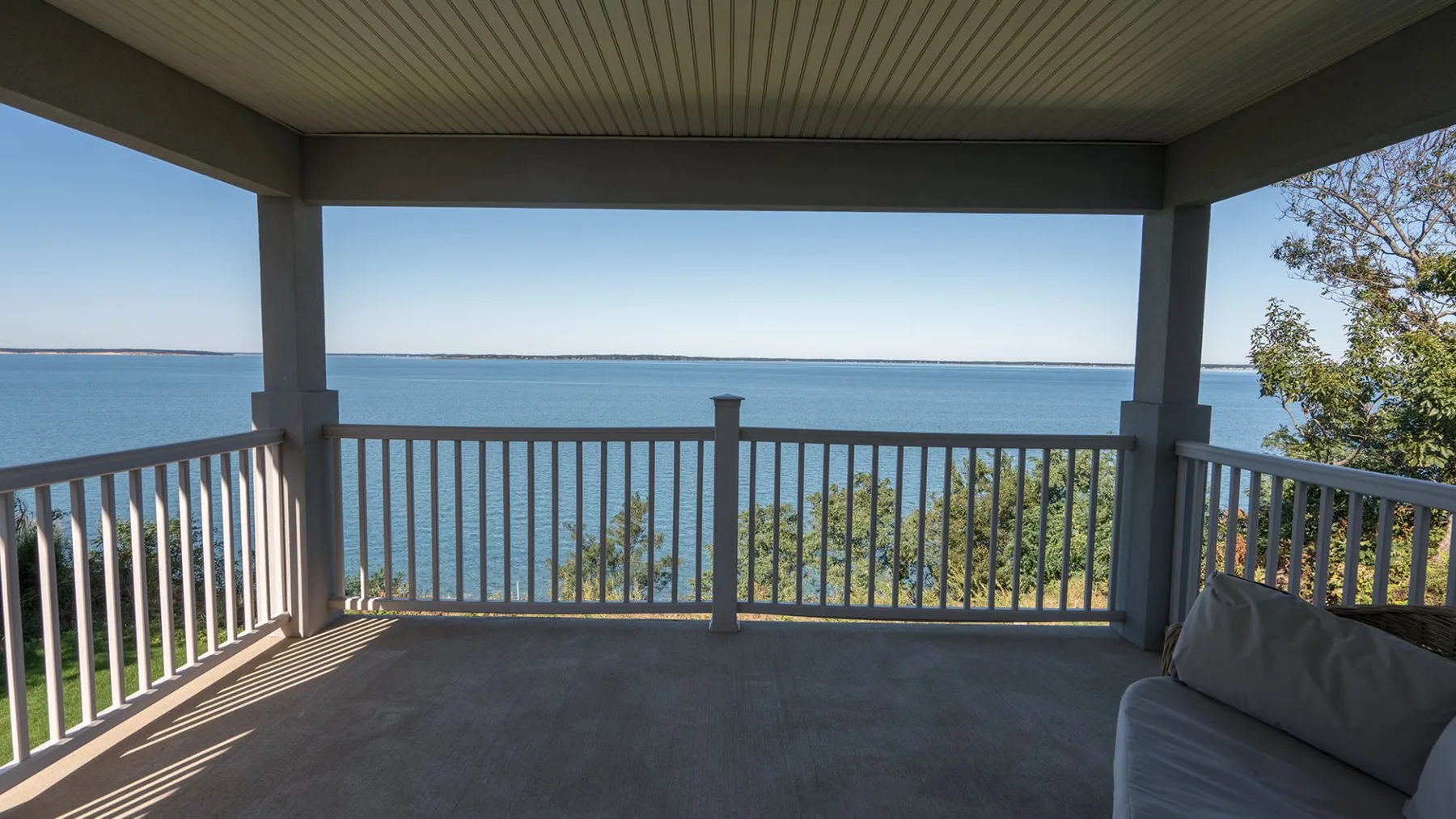 A covered porch overlooks the water, with railing and seating along the side.