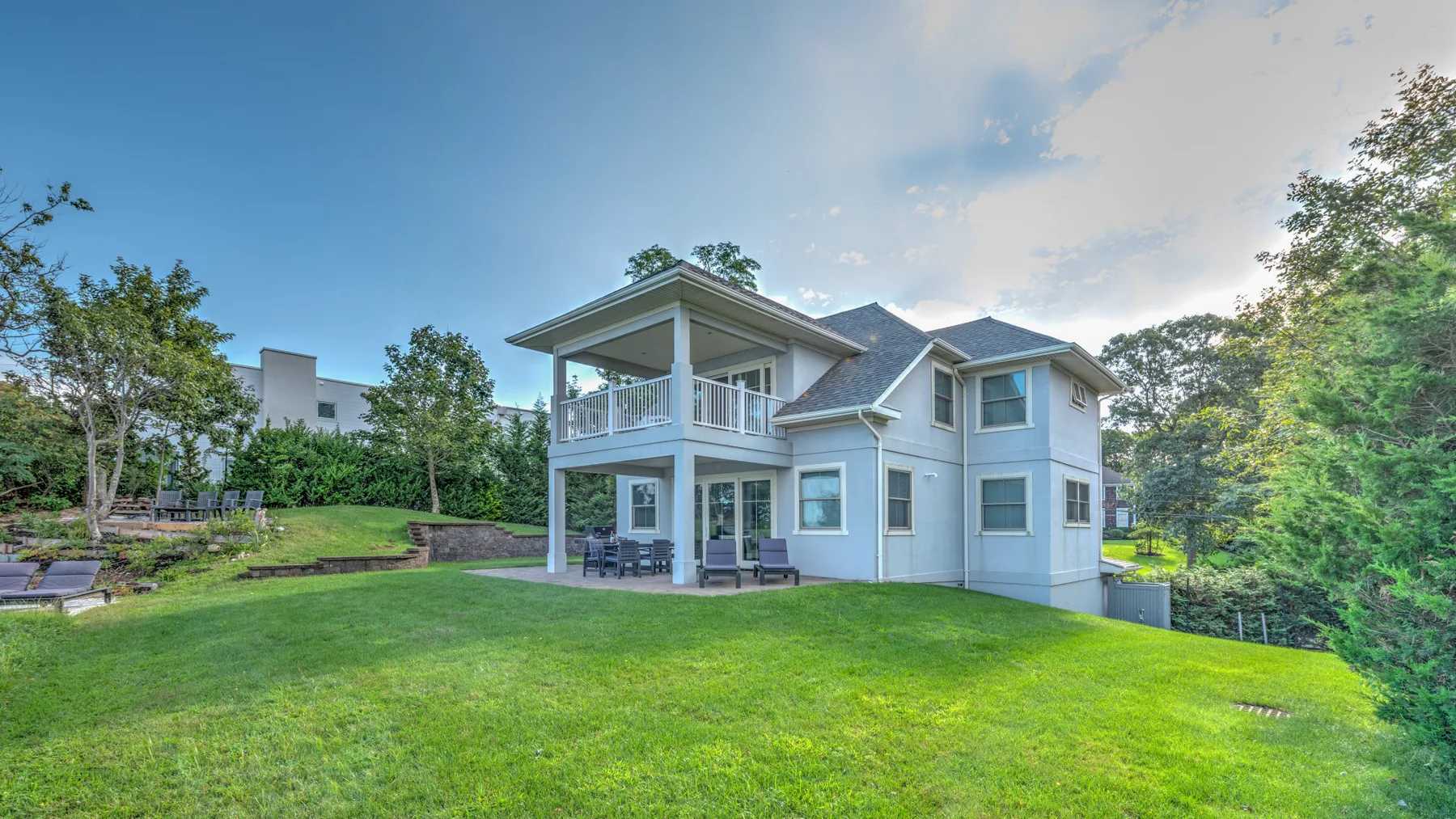 A two-story house with a covered patio overlooks a broad green lawn.