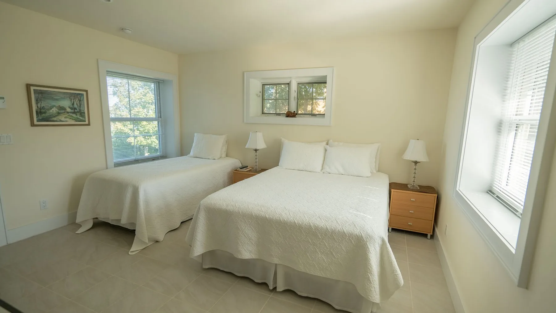 A bright bedroom with two beds and windows letting in daylight.