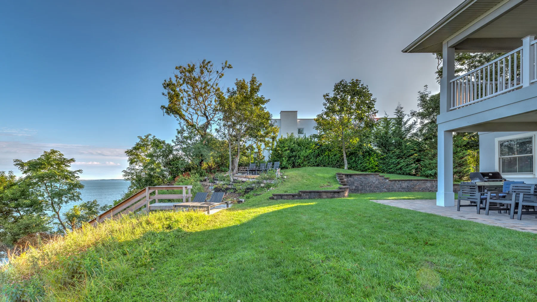 A grassy backyard beside a house overlooks the water.