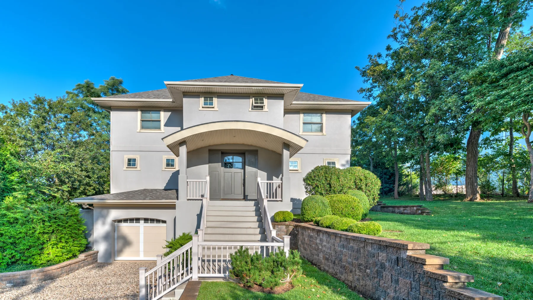 A light-colored two-story house with a curved porch entrance and landscaped yard.