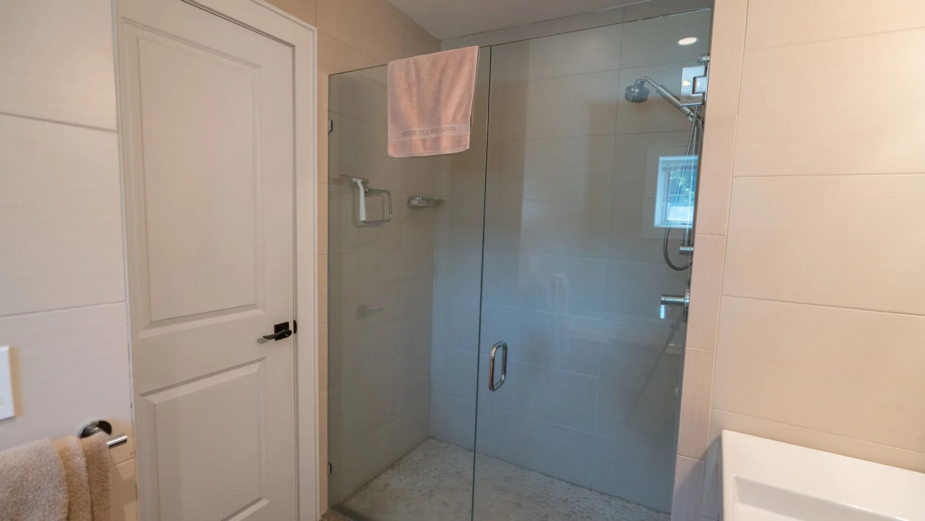 A tiled bathroom with a glass shower and a white door.